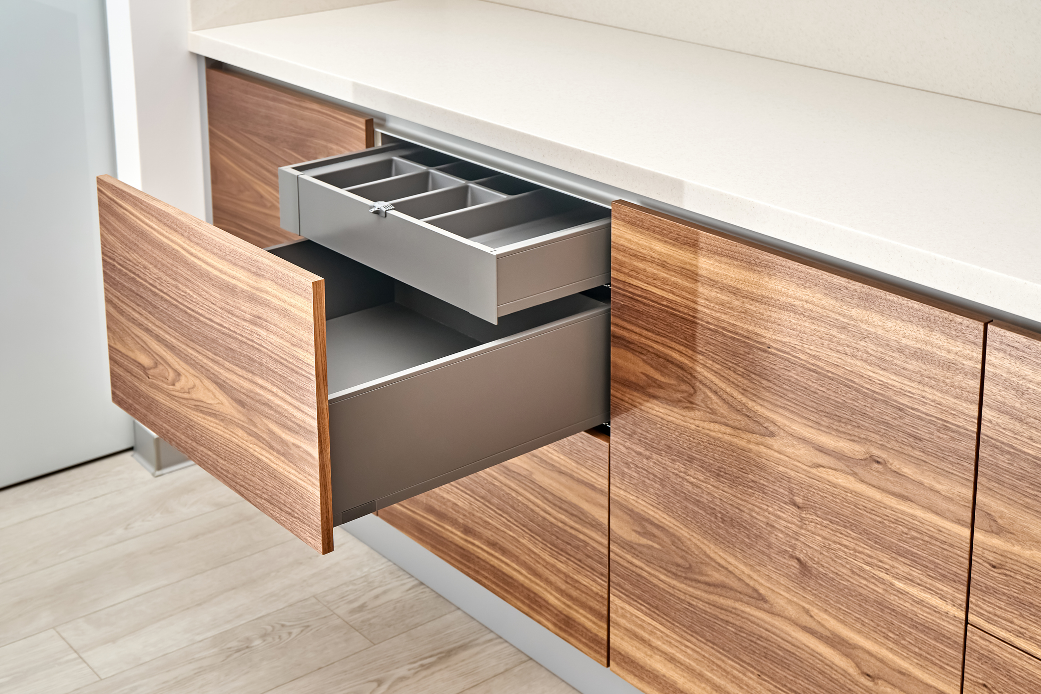 Open drawers of dark grey color with cutlery tray in contemporary cabinet made of walnut wood and gray color with acrylic solid surface countertop close-up